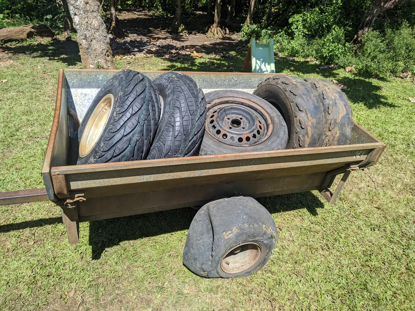 The trailer on the grass with the new tyres and the worn-out old ones in it, and the burst trailer tyre lying in front