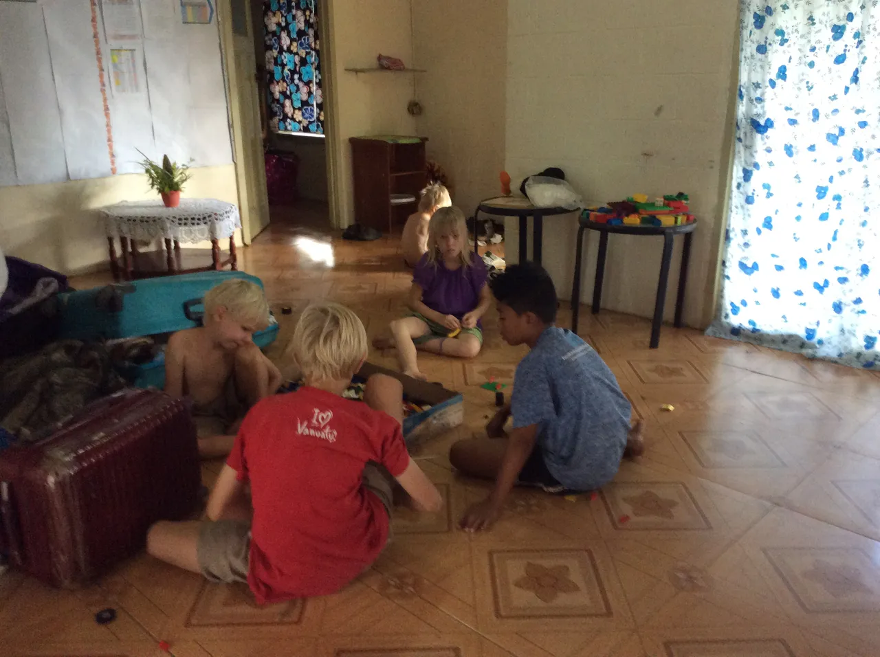 Children playing on the tiled floor of the house in Haʻalalo, next to a suitcase