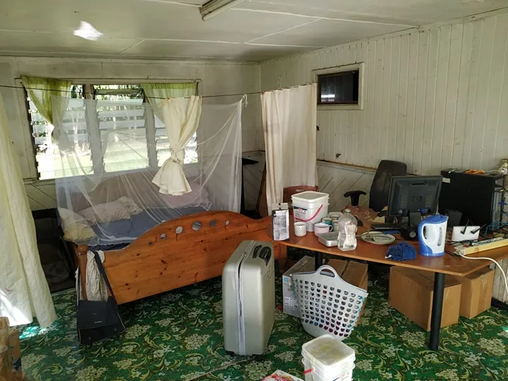 A desk with computers beside a bed with a mosquito net, on a green patterned floor